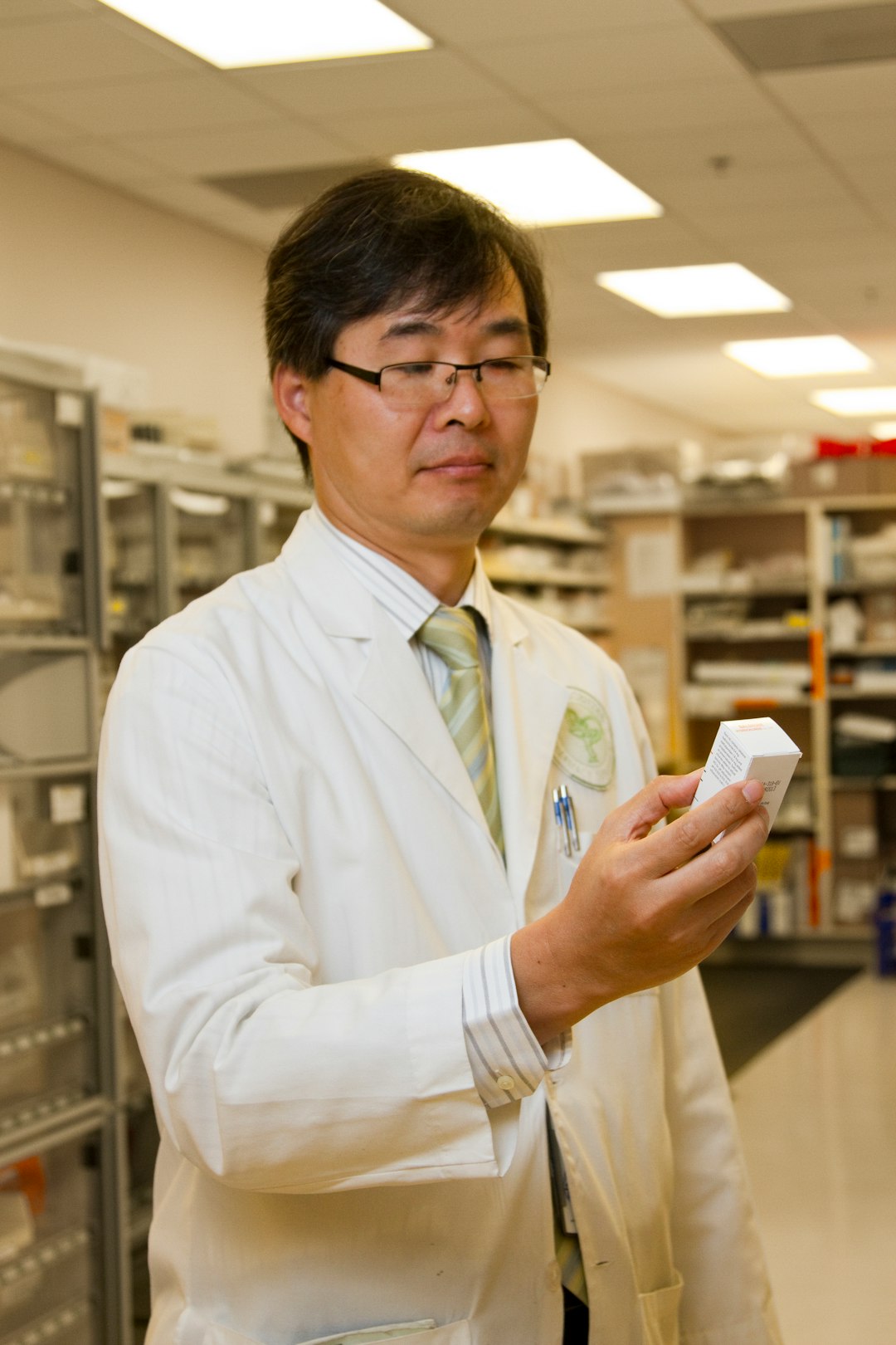 A pharmacist in a white coat examining a medication box in a pharmacy