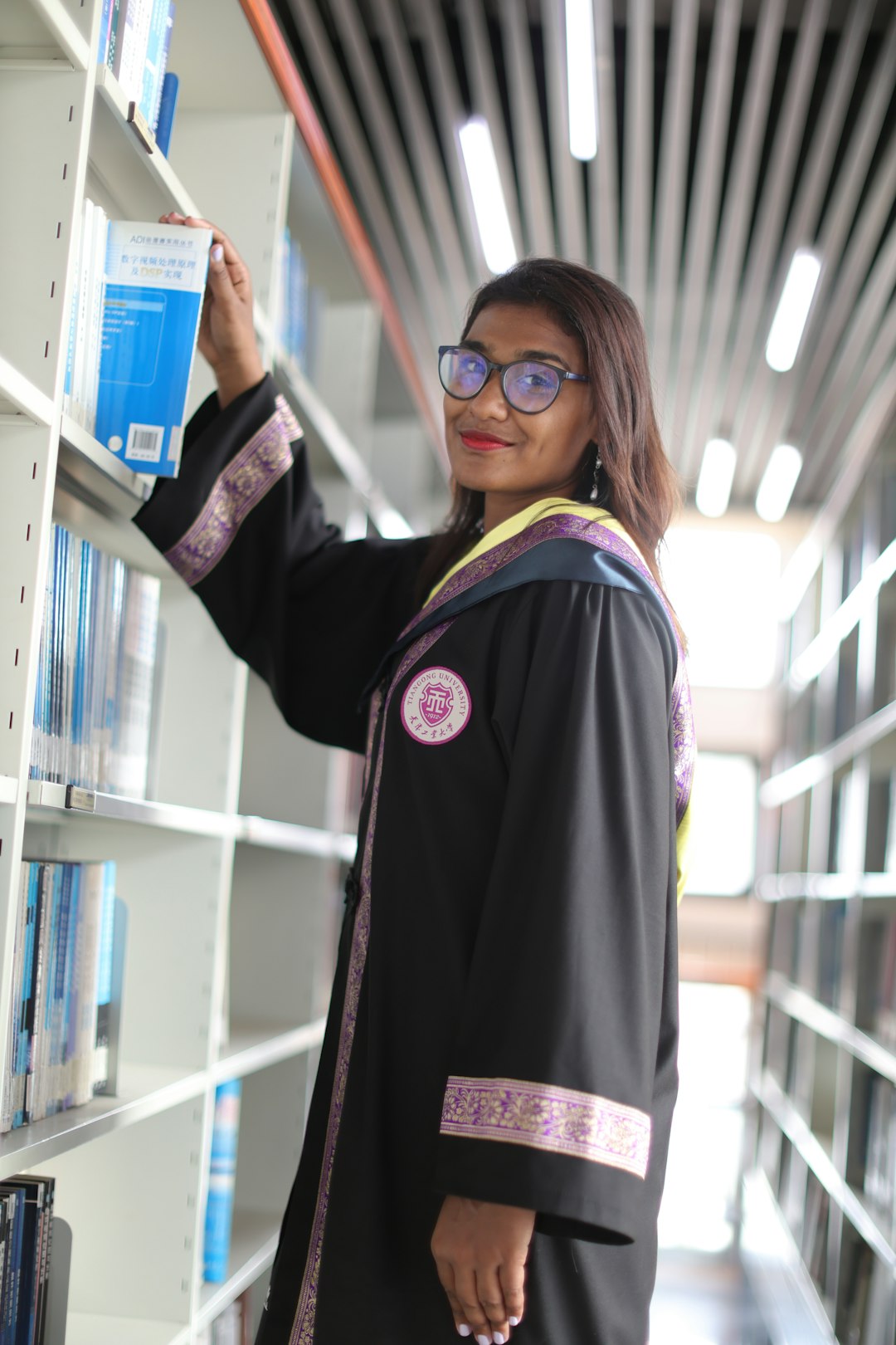 A pharmacy student in a graduation gown shelving books in a university library