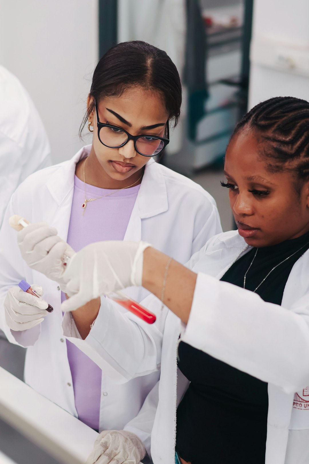 Two pharmacy students in lab coats examining a sample tube together
