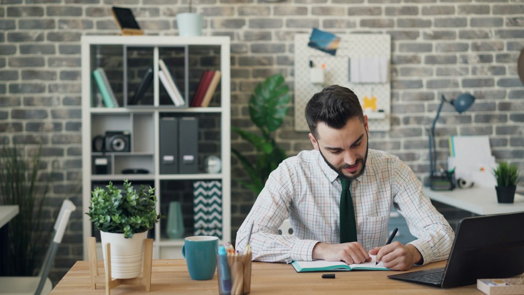 A professional writing in a notebook at an office desk
