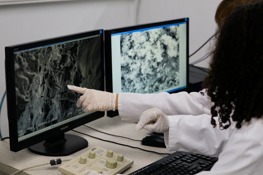 A student in a lab coat pointing to data displayed on a computer screen