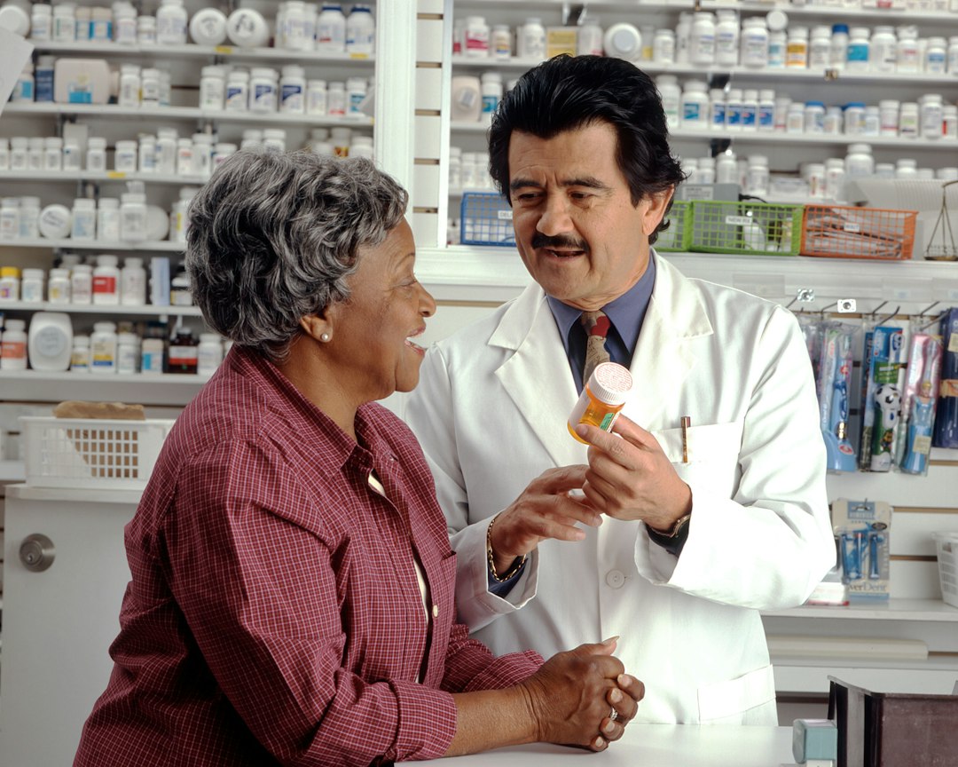 A pharmacist in a white coat consulting with a patient in a pharmacy