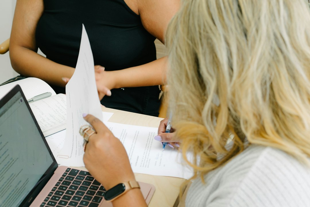 A faculty member reviewing assessment printouts beside a laptop, searching for evidence