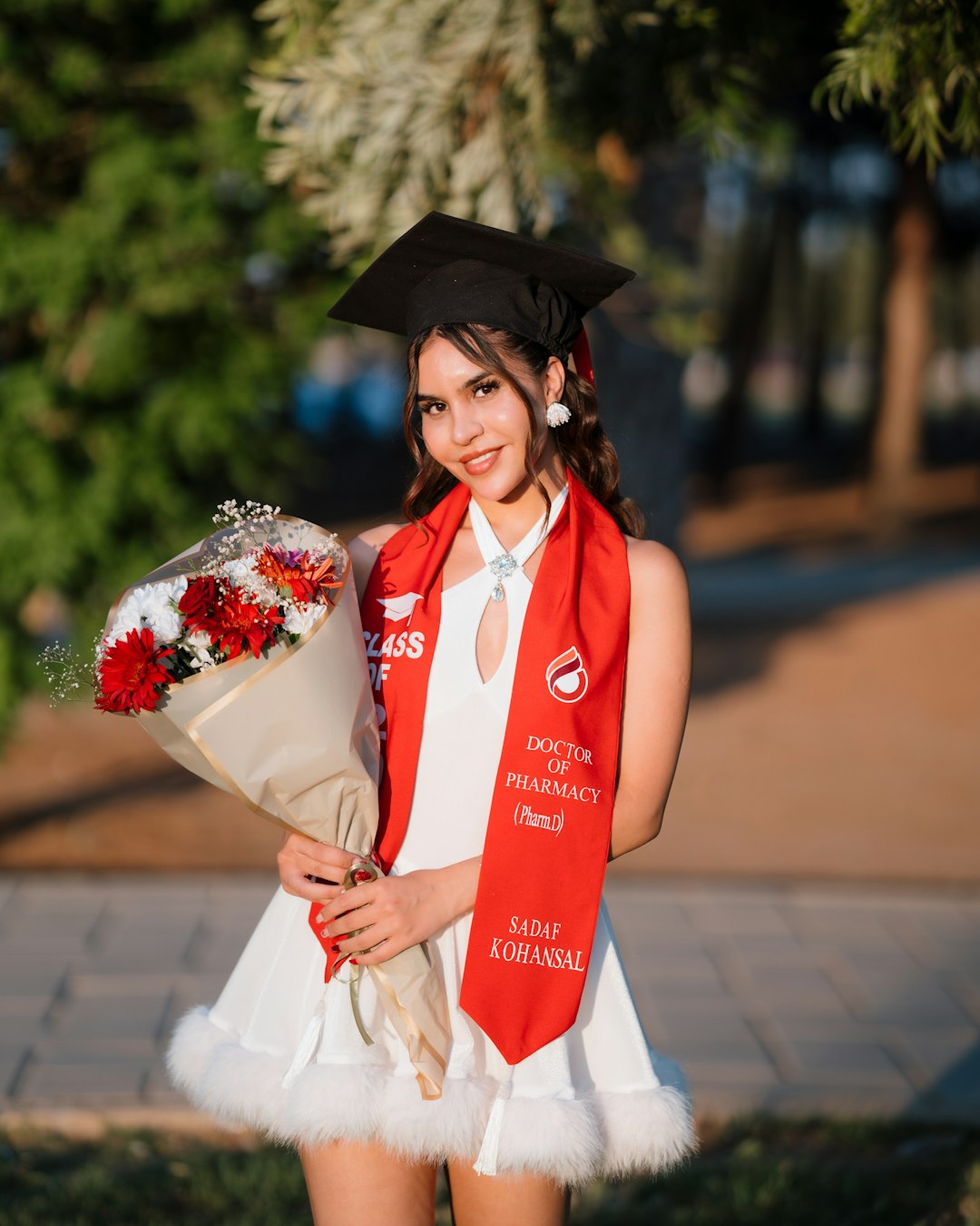 A Doctor of Pharmacy graduate in a red stole holding a bouquet of flowers