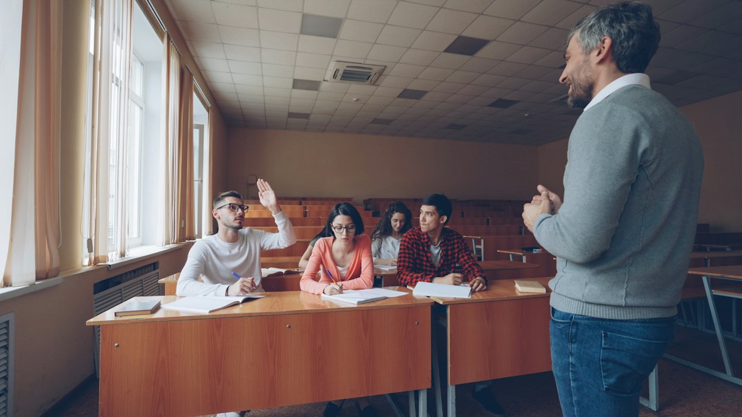 A student raising a hand to a professor in a lecture hall, the kind of curriculum question that exposes an unmapped outcome