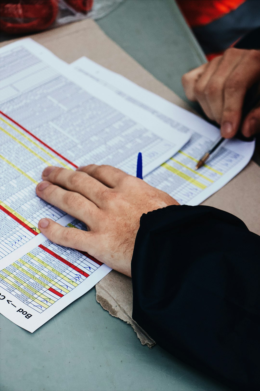 Hands reviewing a data table and forms with pens at a desk