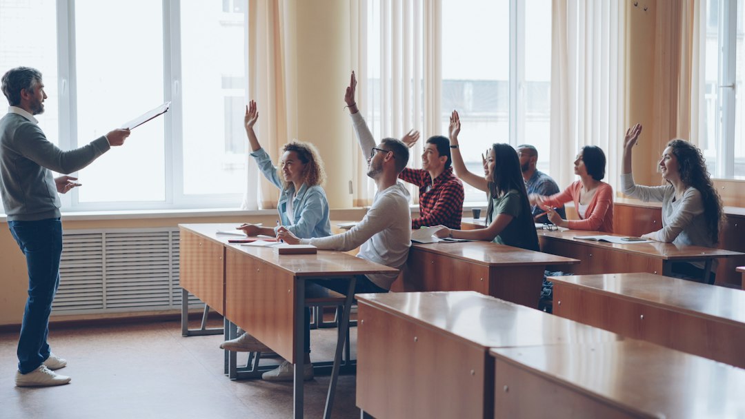 A professor calling on students who are raising their hands in a bright lecture hall